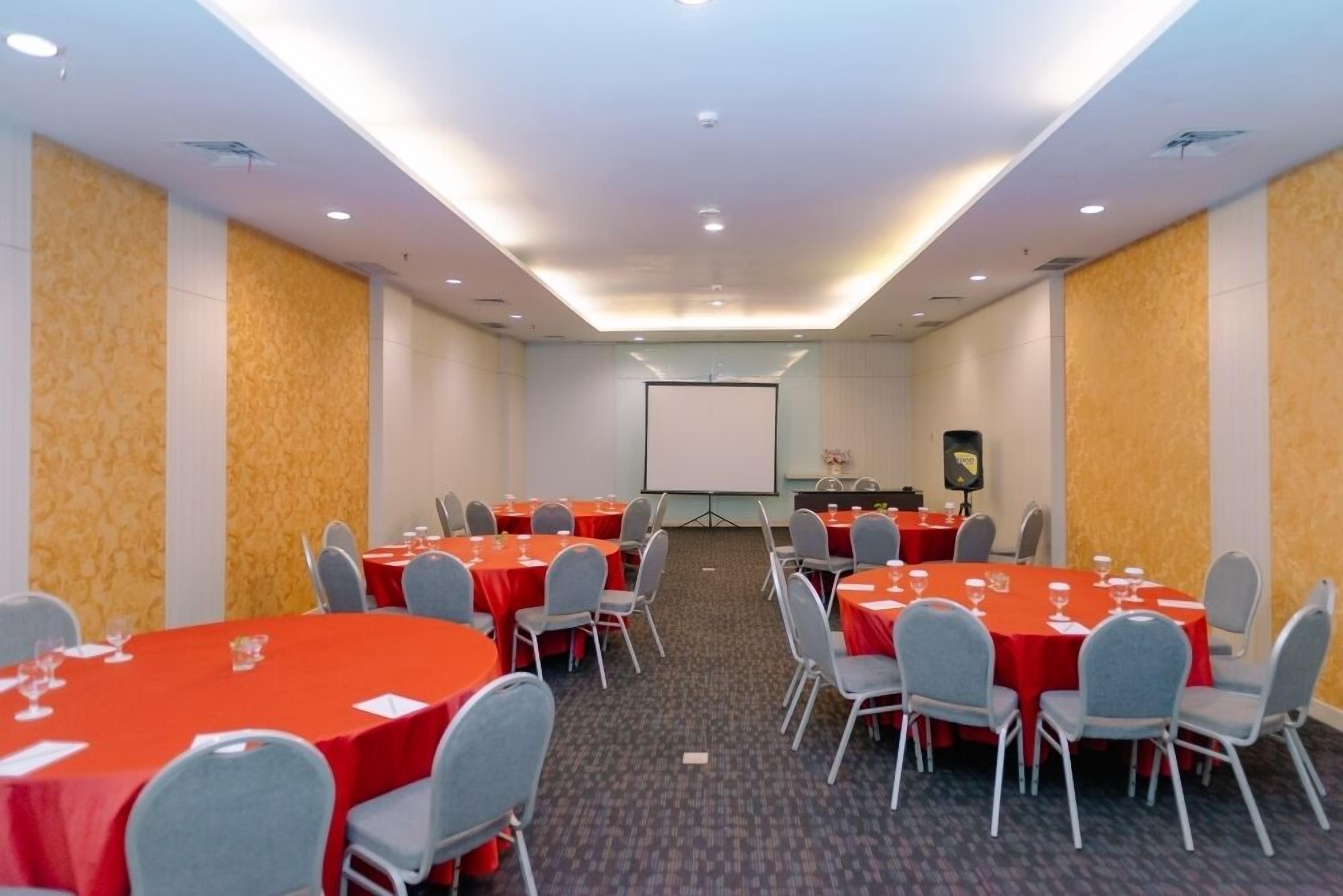 Une salle de conférence avec des tables rondes, des chaises grises et un tableau blanc.