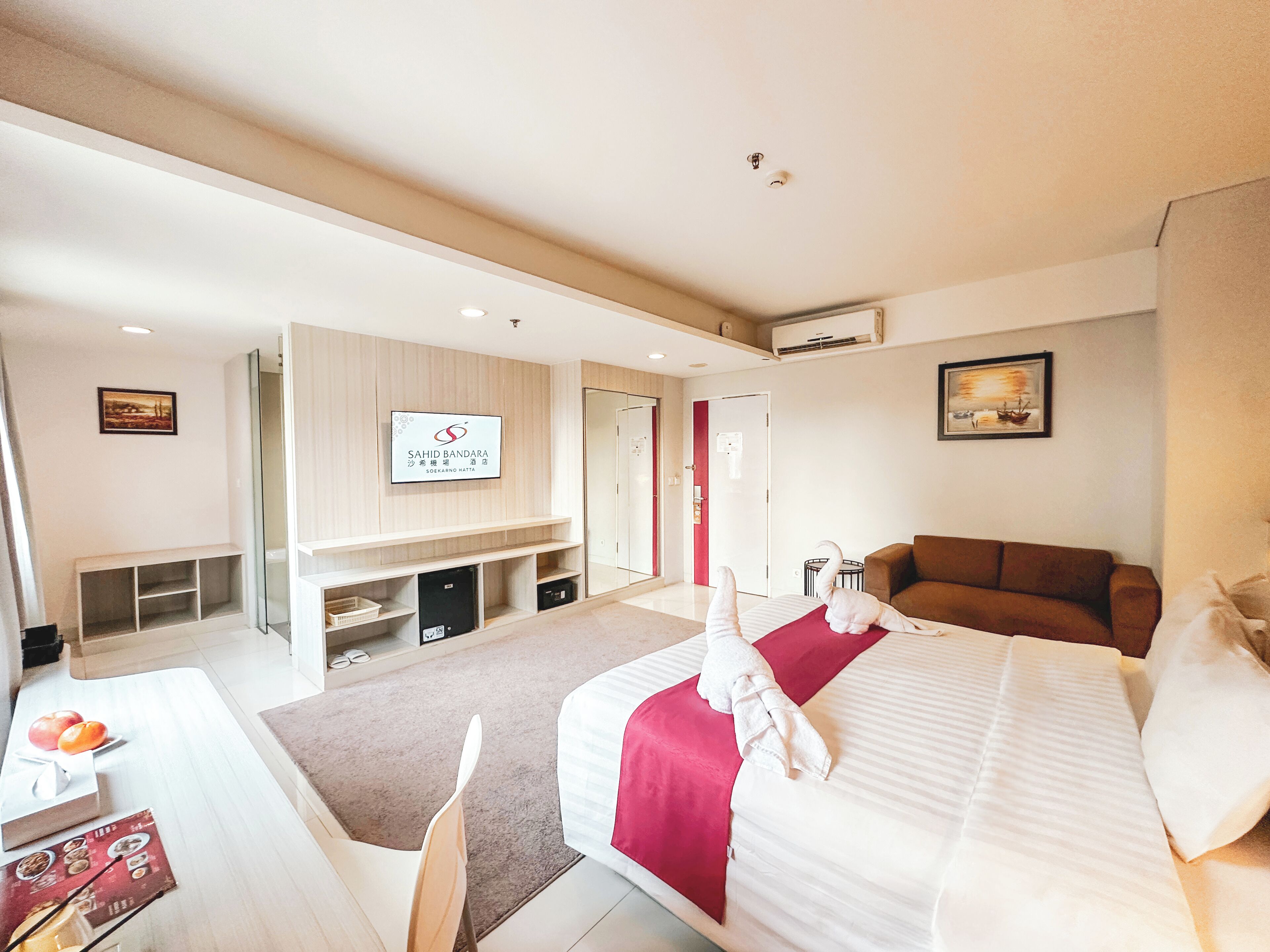 A hotel room with a bed, a TV mounted on the wall, a sofa, and a desk with a chair.