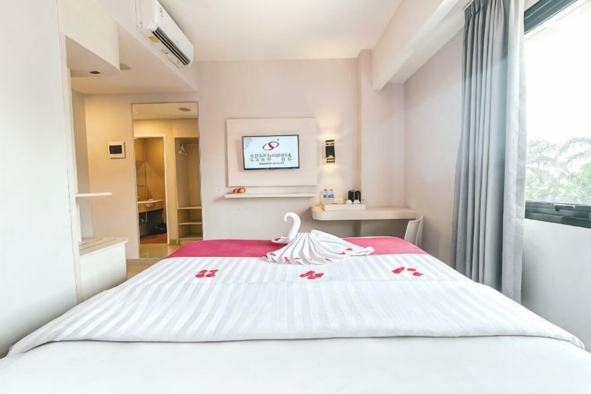 Habitación de hotel con cama, escritorio, espejo y ventana con cortinas.