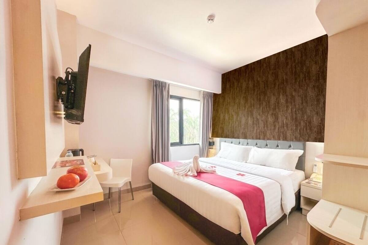 A hotel room with a bed, bedside table, chair, and a desk with a flat-screen TV.