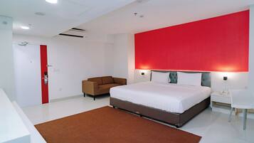 Une chambre d’hôtel moderne avec un grand lit, un mur d’accent rouge, un canapé marron et un bureau blanc.