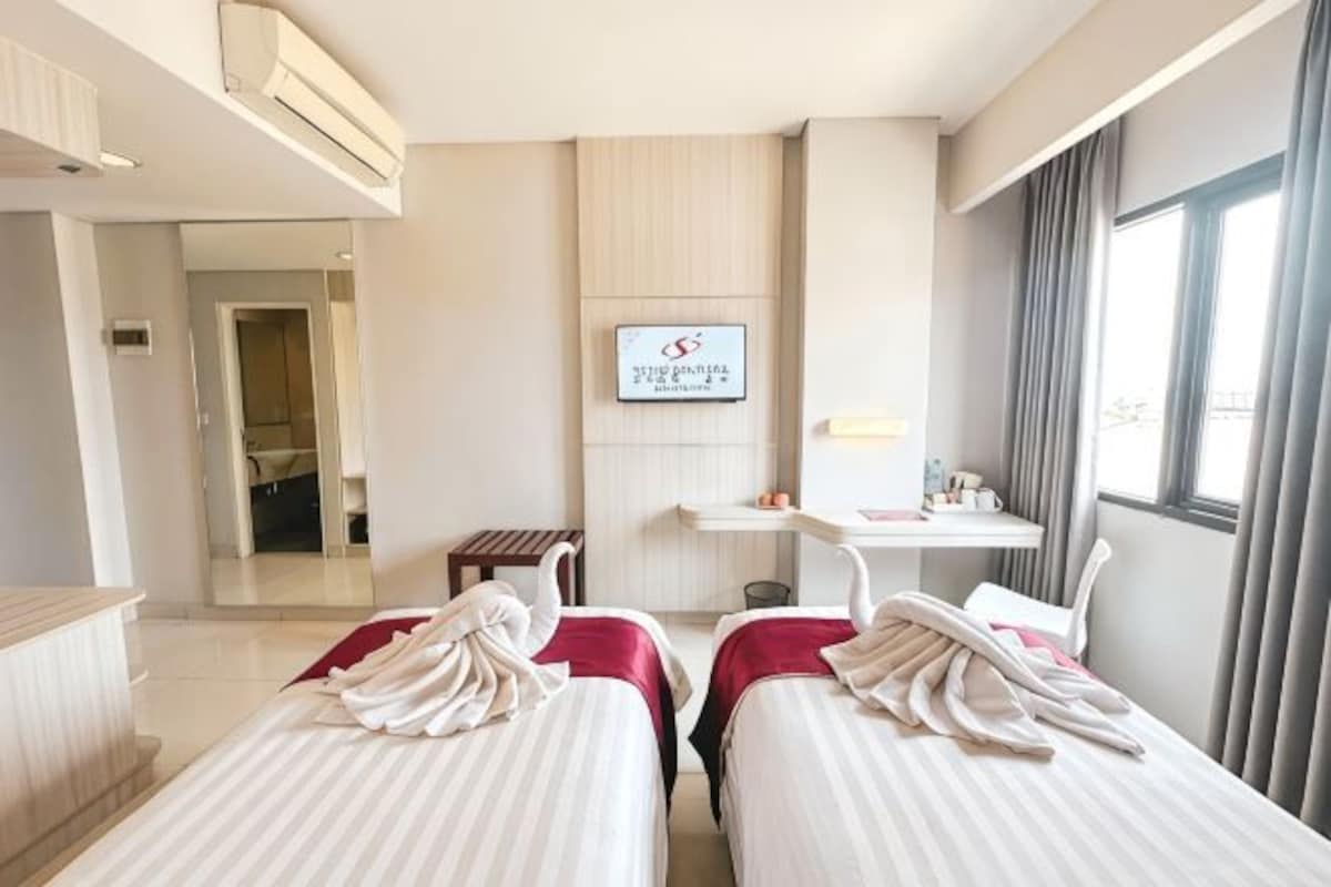 A hotel room with two beds, a TV, a desk, and a window.