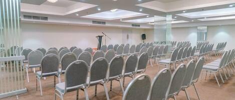 A conference room with rows of grey chairs, a podium, and a speaker on the right side.