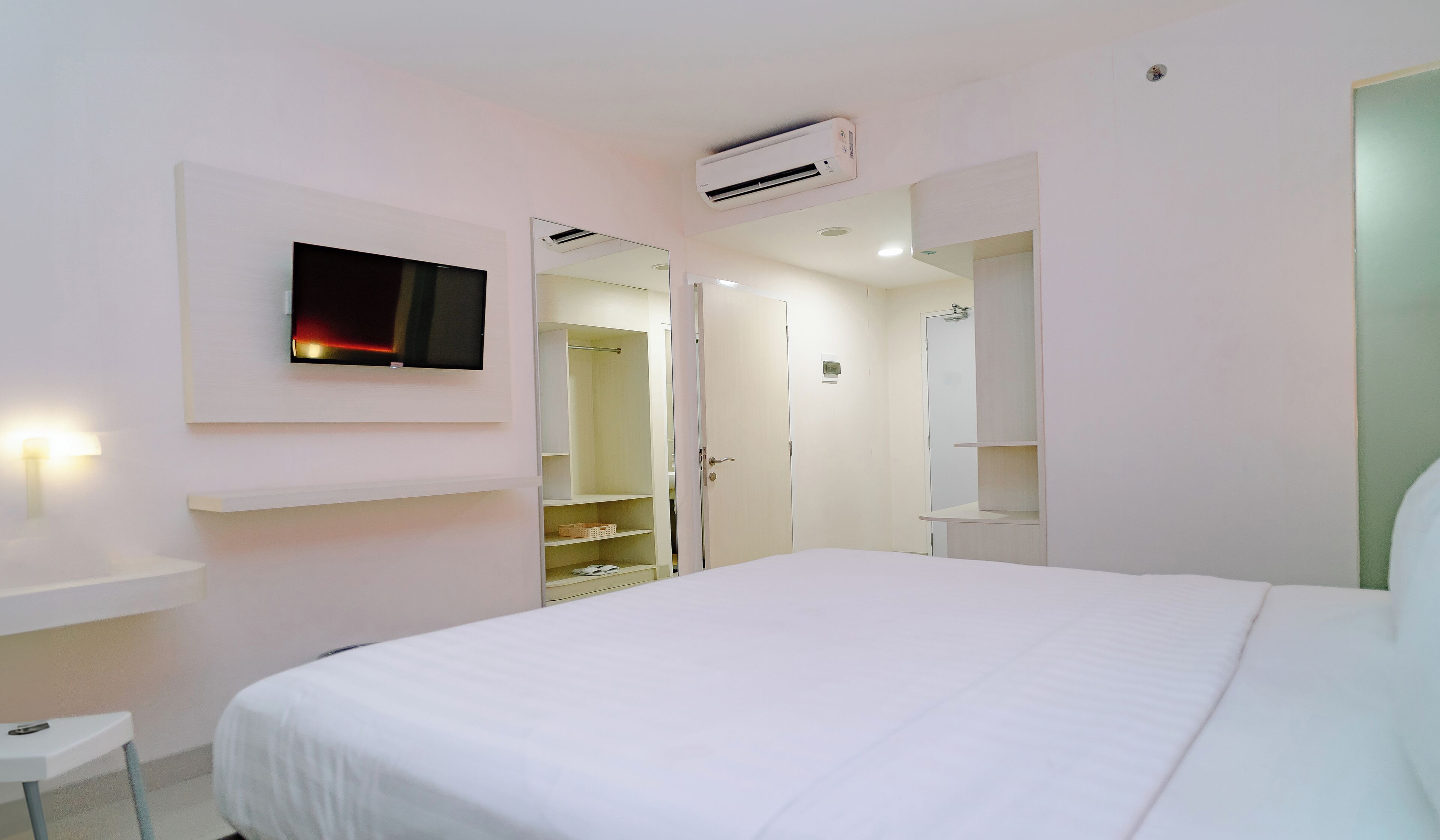 A hotel room with a bed, a TV mounted on the wall, a wardrobe, and a bathroom visible through an open door.