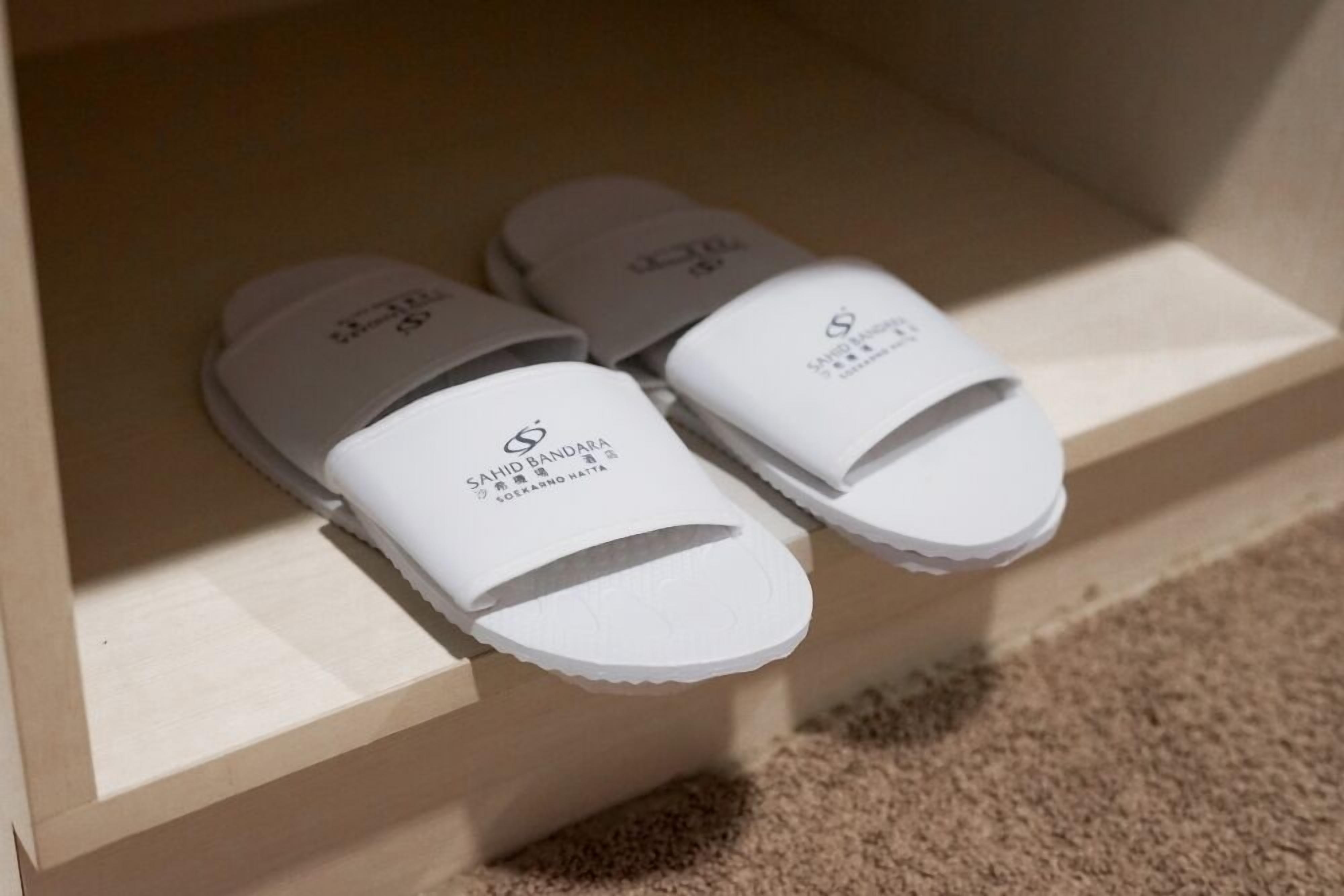 A pair of white slippers with a logo and text on the sole, placed on a wooden shelf.