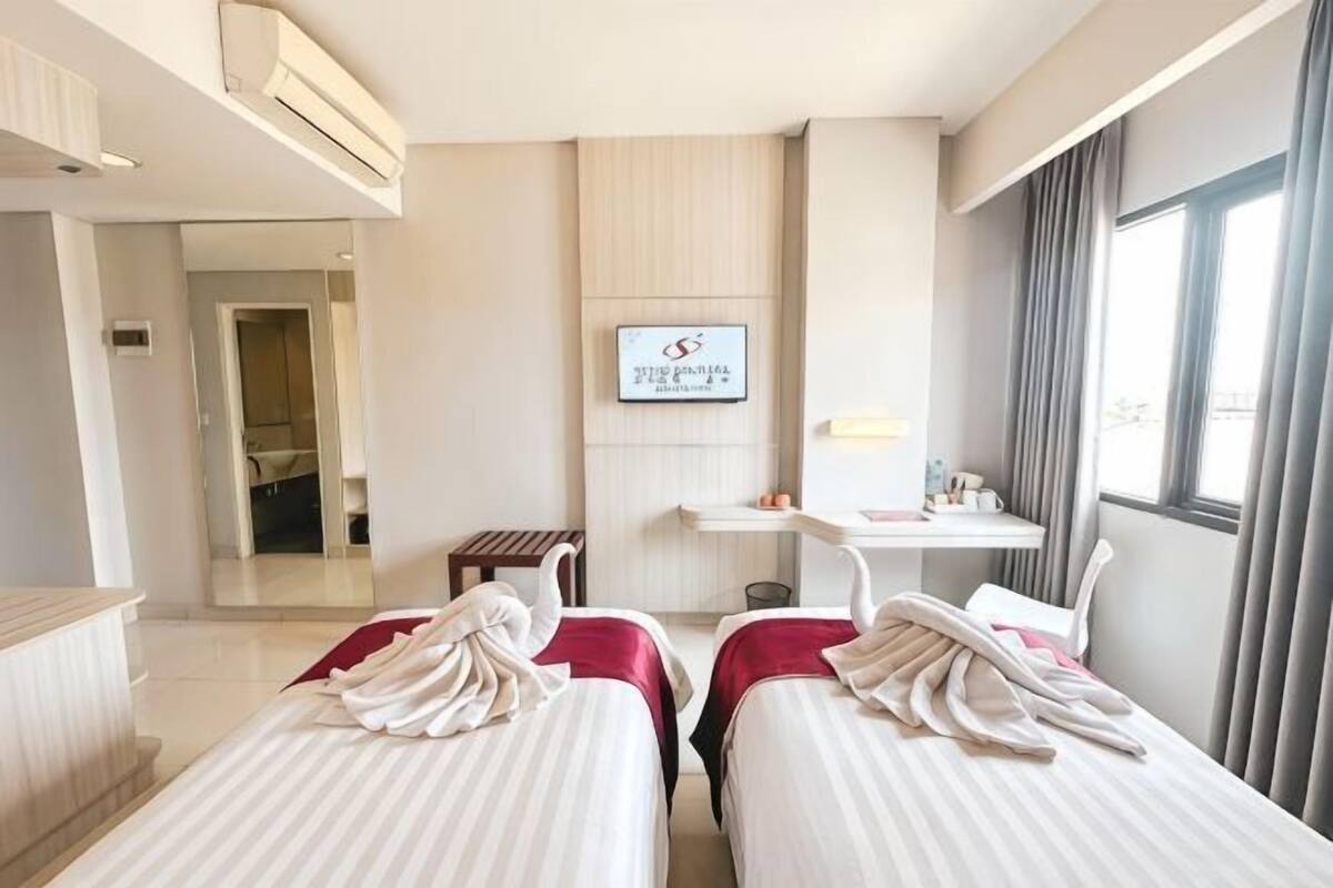 A hotel room with two beds, a TV, a desk, and a window.