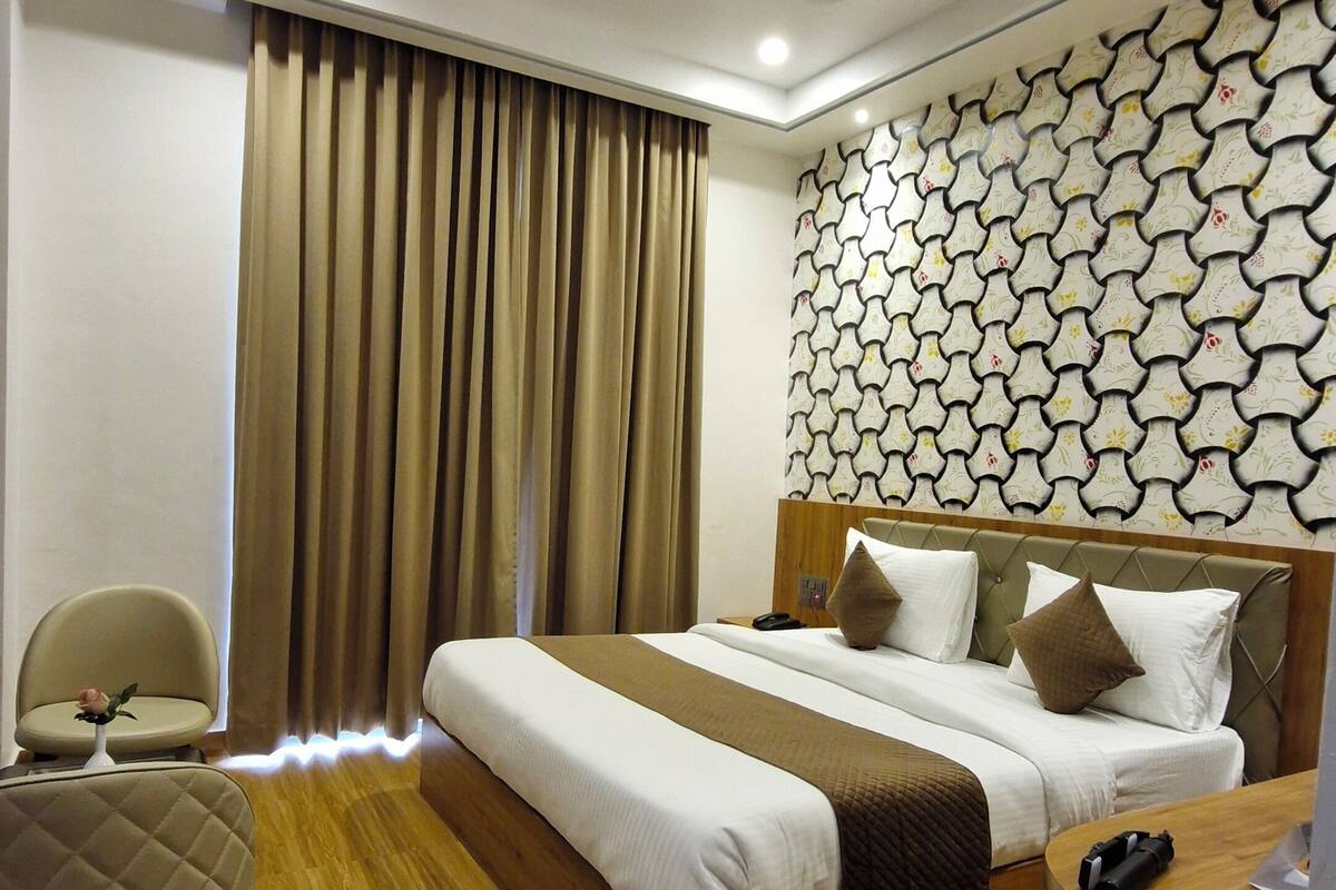 A modern hotel room with a wooden bed, a desk, a chair, and a patterned wall.