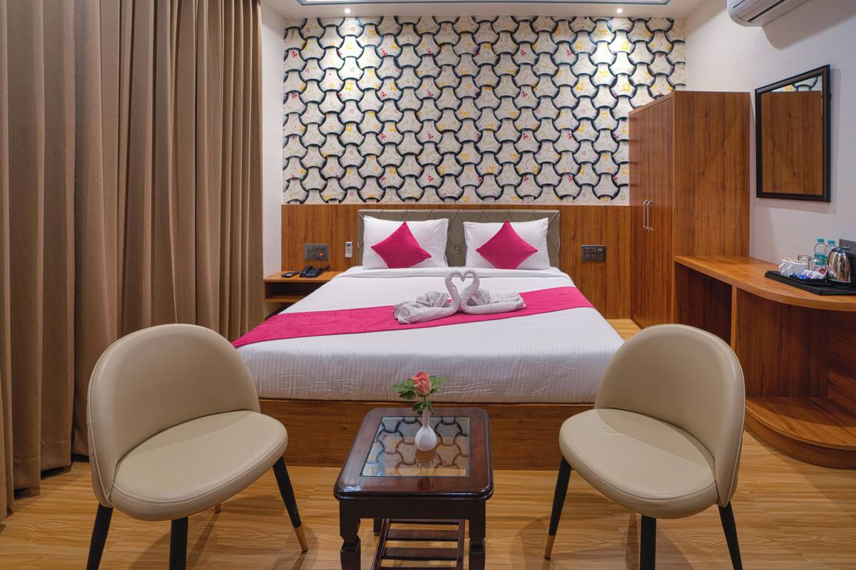 A hotel room with a bed, two chairs, a small table with a vase, and a wooden cabinet.