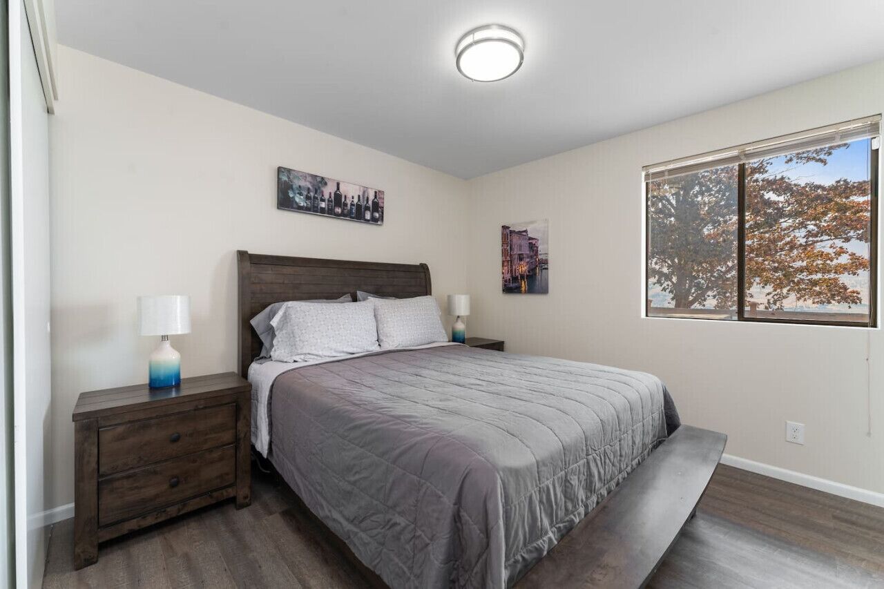 Een slaapkamer met een bed, nachtkastjes, een lamp en een raam met uitzicht op bomen.