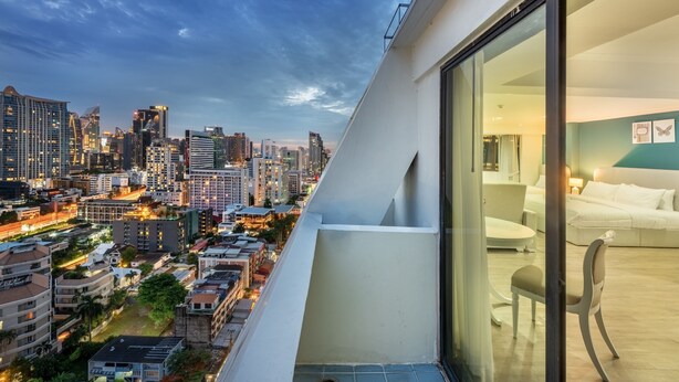 A modern hotel room with a large window overlooking a cityscape at dusk. - Neom Town Residence (Bangkok)