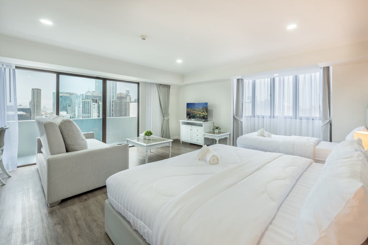 A modern hotel room with a large bed, a sofa, a desk, and a TV.