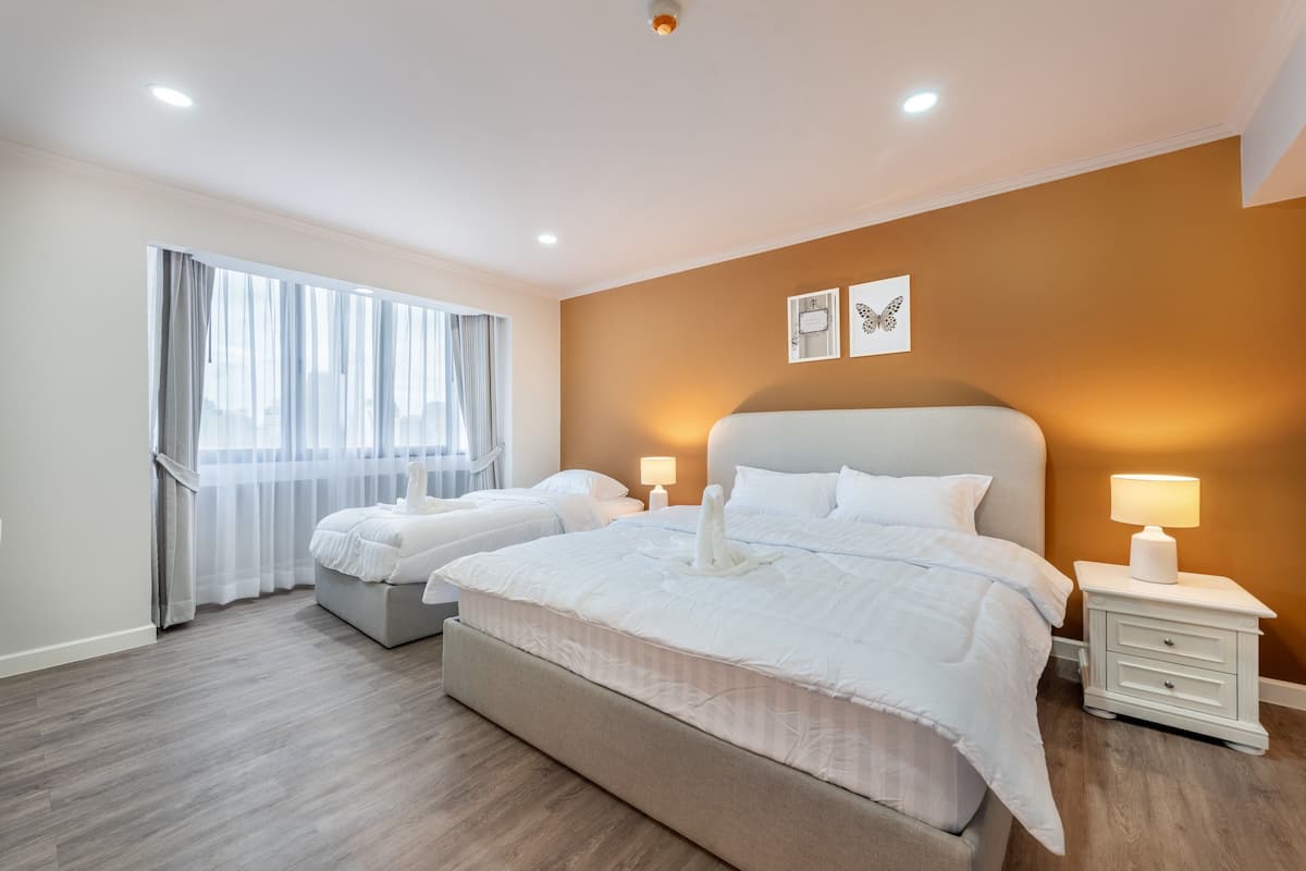 A hotel room with two beds, a large window with sheer curtains, a wall-mounted lamp, and a framed butterfly picture.