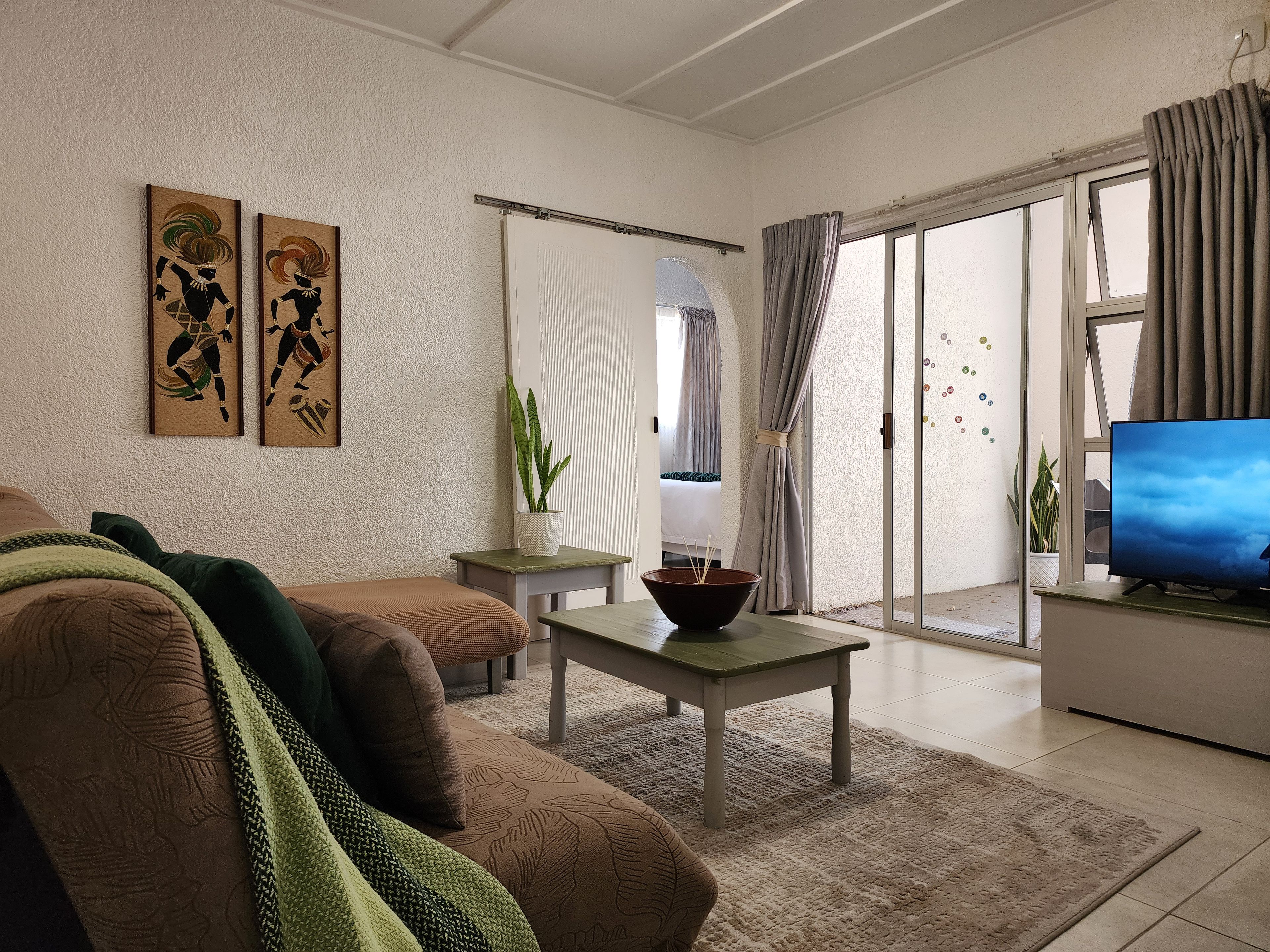 Una sala de estar con un sofá, una mesa de centro, un televisor y un ventanal corredero que da a un balcón.