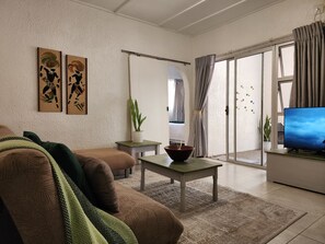 Ein Wohnzimmer mit einer Couch, einem Couchtisch, einem Fernseher und einer Glastür, die auf einen Balkon führt.