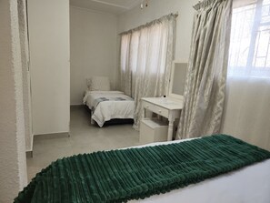 Ein Schlafzimmer mit einem Bett, einem Nachttisch, einem Spiegel und einem Fenster mit Vorhängen.