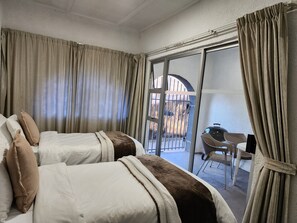 Habitación de hotel con dos camas, un balcón con vistas y un comedor con sillas y una mesa.