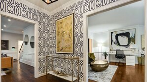 A spacious living area with a wooden floor, a decorative wall panel, a large abstract painting, a modern desk, and a round brass table. - Buckhead 4-BDM/3.5 Bath, chic house, w baby grand Piano. Mins to Shopping/Gov Mn (Atlanta)