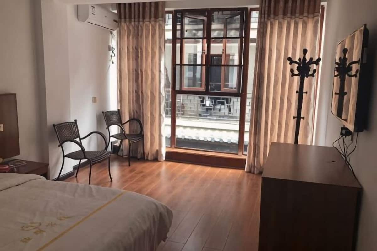 Une chambre d’hôtel comprenant un lit, deux chaises, un bureau, une fenêtre avec des rideaux et un téléviseur fixé au mur.