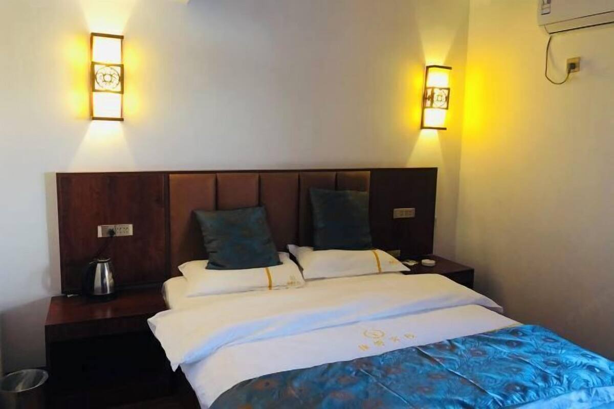 Une chambre d’hôtel avec une tête de lit en bois, deux tables de chevet, un lit avec une literie blanche et une couverture à motifs bleus, ainsi que deux appliques murales.