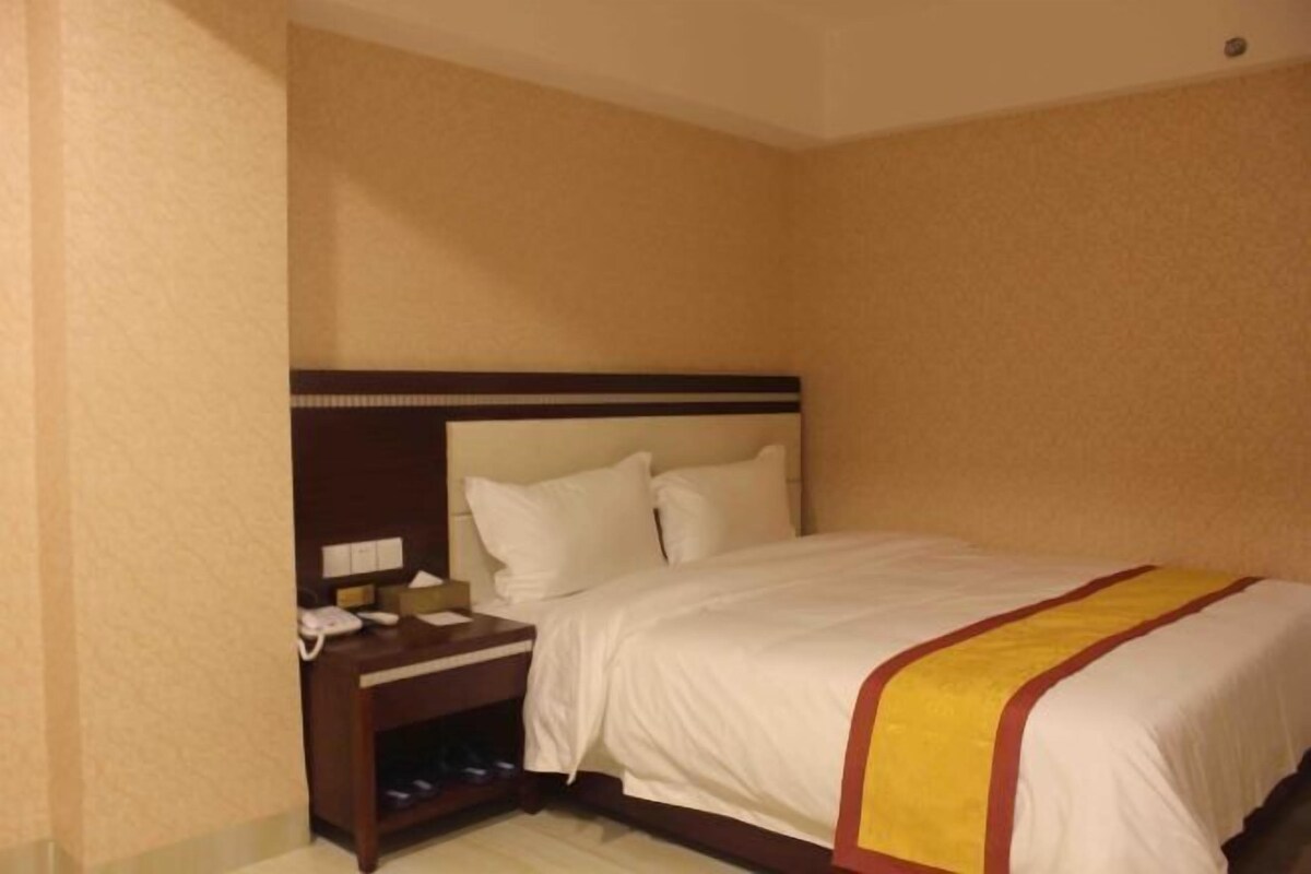 A hotel room with a bed, a nightstand with a phone, and a small shelf.