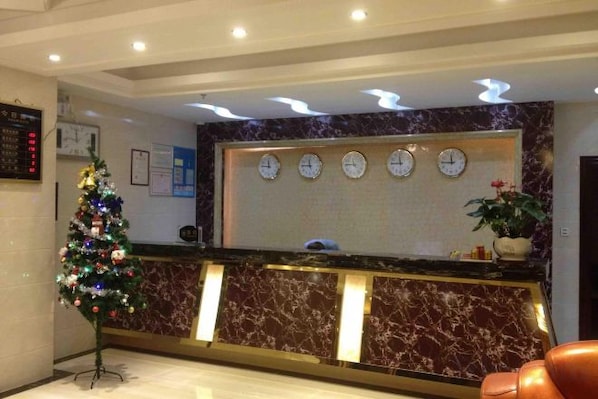 Uma área de recepção de hotel com balcão de mármore, árvore de Natal e relógios na parede.