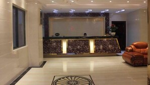 Zona de recepción de un hotel con mostrador de mármol, una araña y un sillón de cuero.