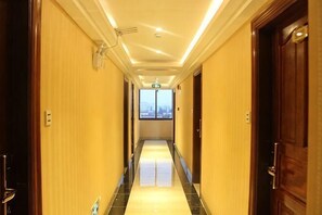 A hotel corridor with doors on both sides, a tiled floor, and a view through the end of the corridor. - JUNTING HOTEL (Zhanjiang)