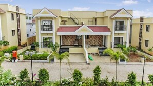 A multi-story residential building with a central entrance, balconies, and a tiled roof. - 3BHK w/Pool - Sunset Palazzo by Universe Villas (Karjat)