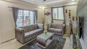 A living room with two grey sofas, a glass coffee table, and a ceiling fan. - 3BHK w/Pool - Sunset Palazzo by Universe Villas (Karjat)