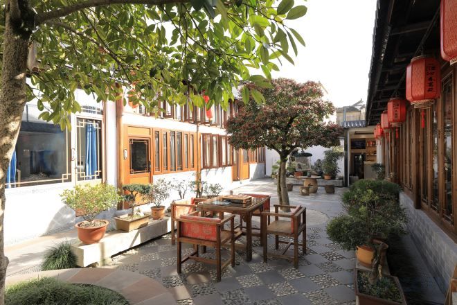An outdoor seating area with tables and chairs, surrounded by potted plants and a tree.