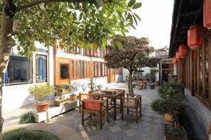 Un área de estar al aire libre con mesas y sillas, rodeada de macetas con plantas y un árbol.