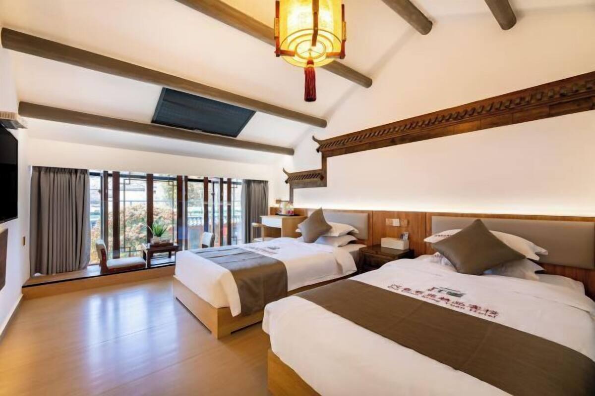 Habitación de hotel con dos camas, televisión, un ventanal grande y una lámpara de techo de estilo tradicional.