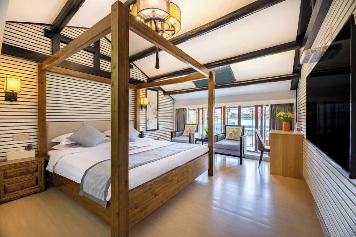 Un dormitorio con cama con dosel, cabecera de madera, mesitas de noche, un escritorio y un ventanal grande.