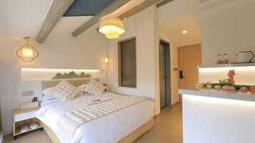 Un dormitorio moderno con cama, mesitas de noche, un banco empotrado, luz de techo y una pequeña zona de kitchenette con encimera y objetos decorativos.