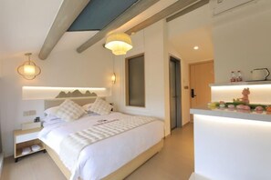 Un dormitorio moderno con cama, mesitas de noche, un banco empotrado, luz de techo y una pequeña zona de kitchenette con encimera y objetos decorativos.