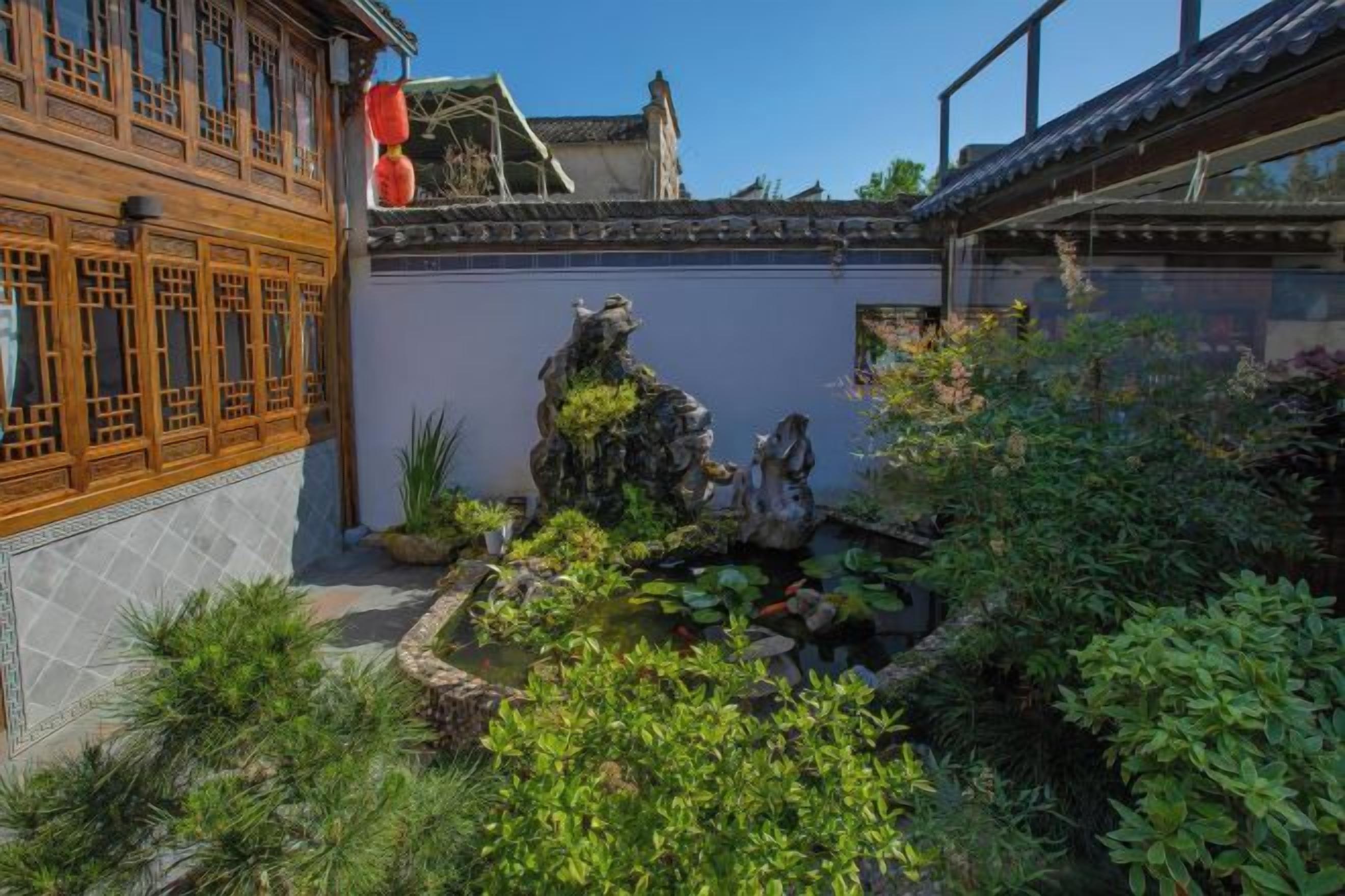 A traditional courtyard with a wooden building, a rock garden, and a pond.
