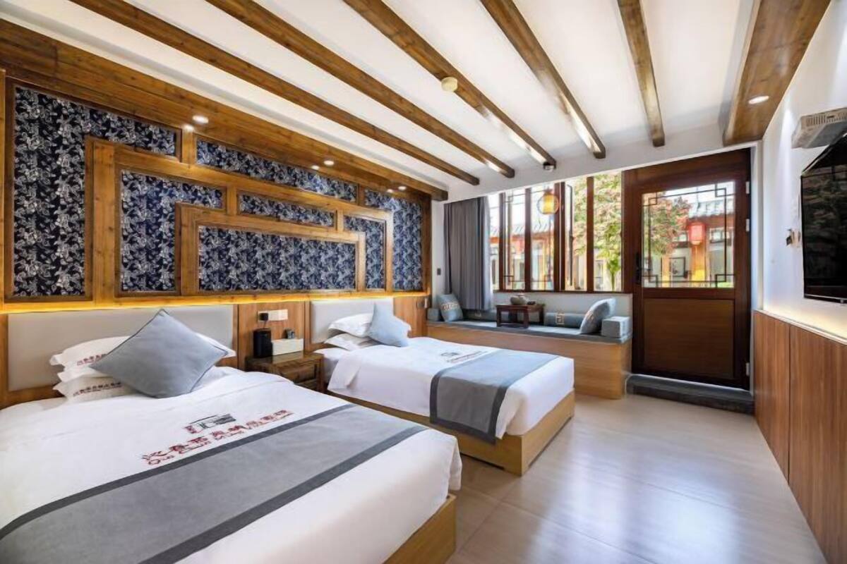 Habitación de hotel con dos camas, techo de madera, pared con diseño, zona de estar y televisor.
