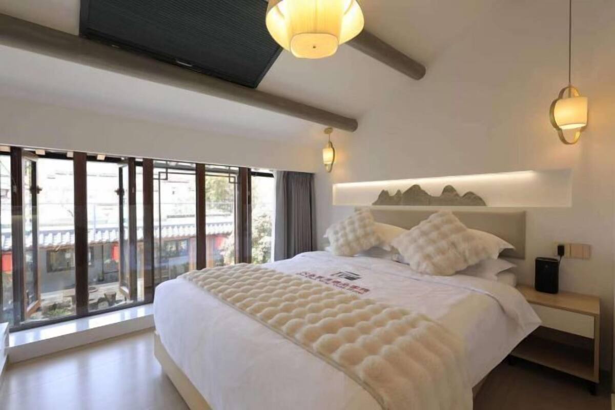 Una habitación de hotel moderna con una cama grande, una mesita de noche y vistas al exterior por una puerta corredera.