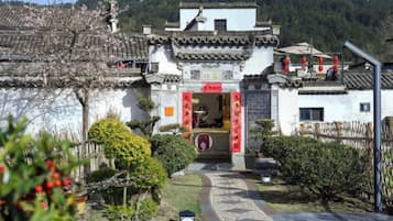 A traditional building with a tiled roof, a central entrance with red decorations, and a pathway leading to it.