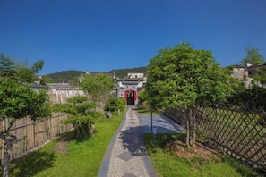 Un chemin menant à un bâtiment traditionnel avec une porte rouge, entouré de verdure et d’une clôture.
