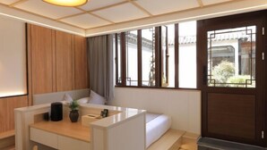 A modern hotel room with a wooden desk, a sofa, and a large window with a view of the outside.