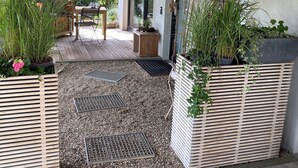 Un patio techado con terraza de madera, una mesa y sillas, y macetas con plantas.