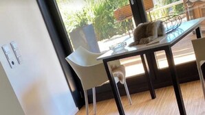 Una habitación con una cama, una mesa y un gato, y una ventana con vistas a la vegetación.
