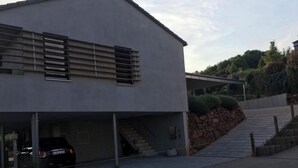 Un edificio moderno con una zona de estacionamiento techada y una escalera que sube por la ladera.