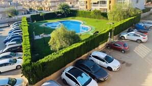 Un quartier résidentiel doté d’une piscine, entourée de haies bien entretenues, et bordé d’une rangée de voitures garées.