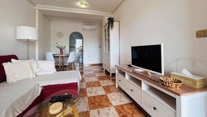 Un salon avec un canapé, un téléviseur, une table basse et, au fond, un coin repas.