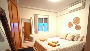 Une chambre à coucher avec un lit, une fenêtre avec des rideaux, un miroir et un climatiseur fixé au mur.