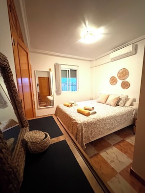 A bedroom with a bed, a window with curtains, a mirror, and a wall-mounted air conditioner.