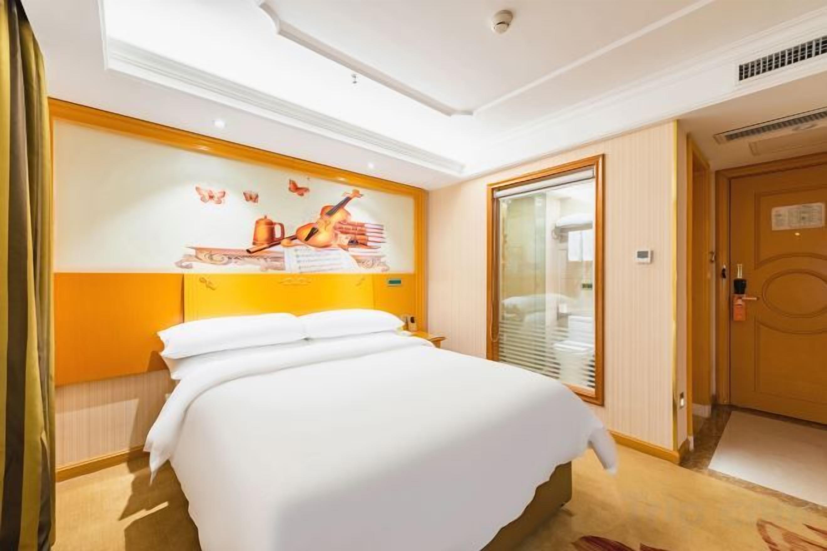 A hotel room with a large bed, a wall-mounted artwork, a door with a sign, and a carpeted floor.