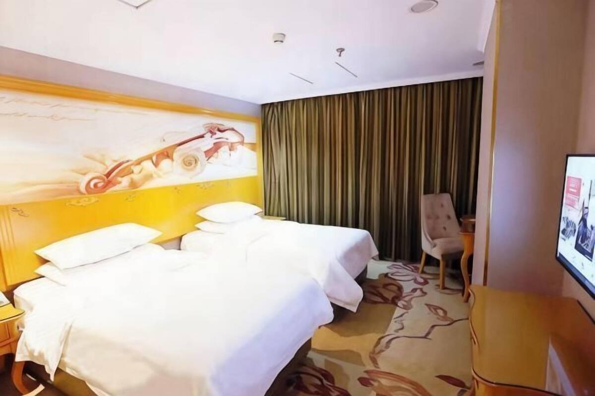 A hotel room with two beds, a television, a desk, and a curtain.